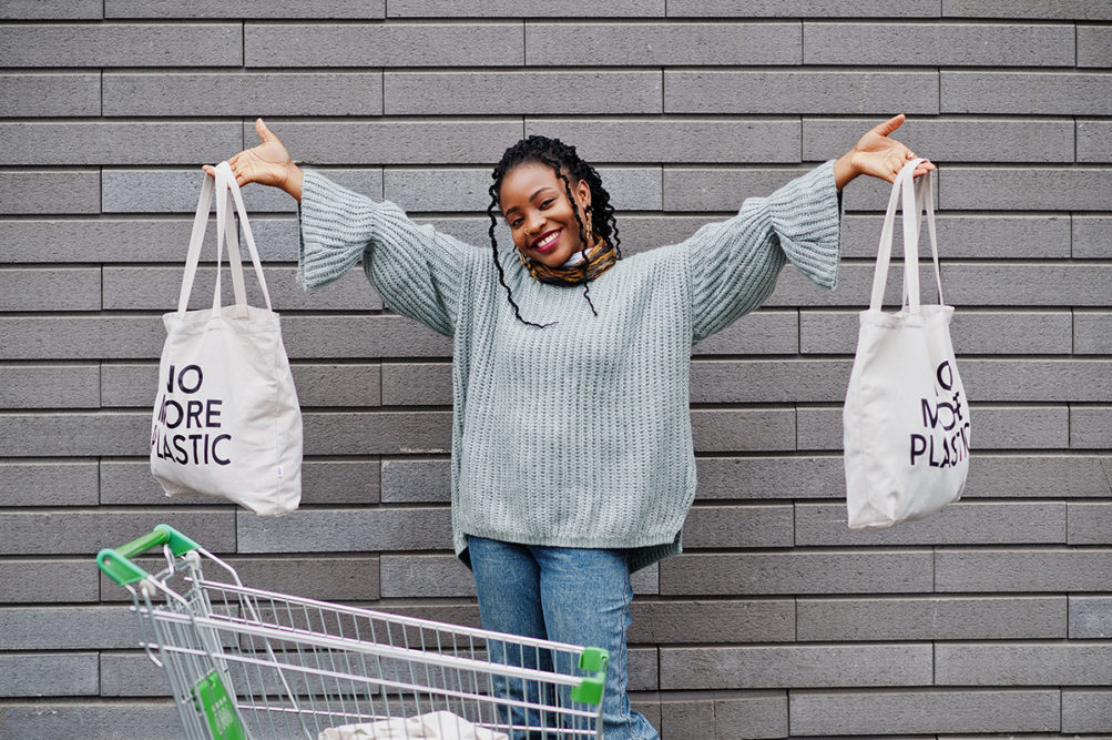 Young woman with shopping cart and eco bags posed outdoor market