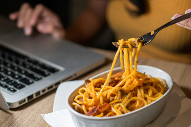 Woman working from home eats a bowl of spaghetti while working. 