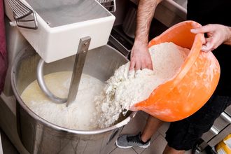 Baker adding flour to dough