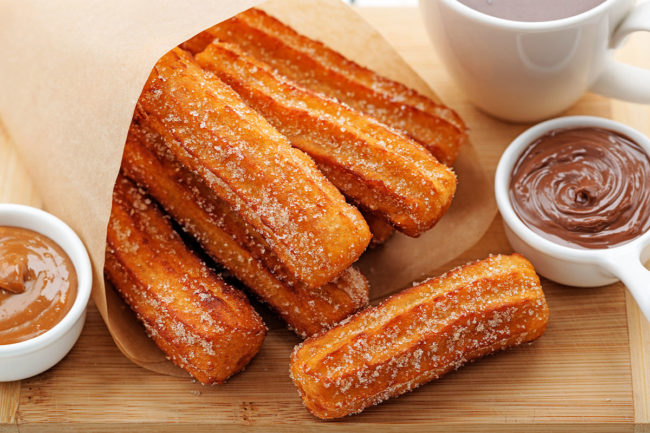 Bag of churros with a side of chocolate sauce. 